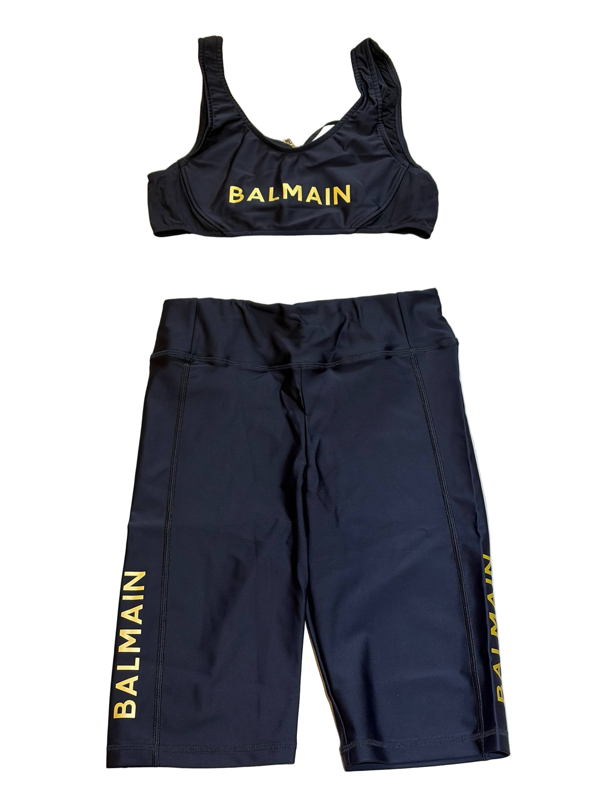 Black sports bra and shorts set with 'Balmain' branding on a light wooden floor.
